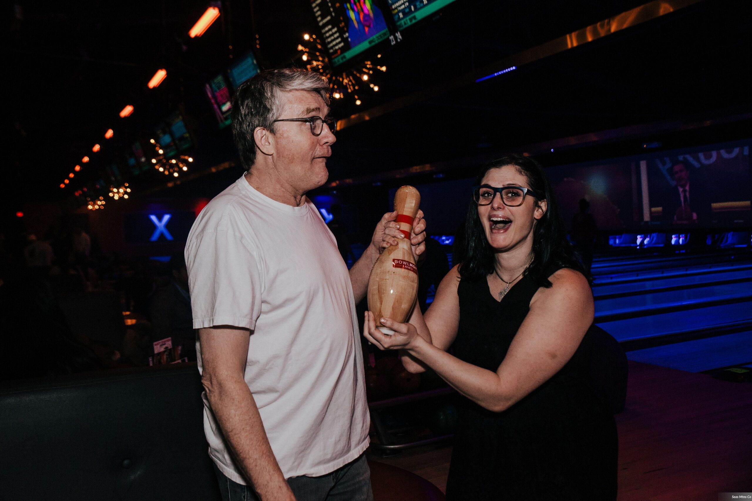 Bride and Groom making funny faces holding bowling pin at Bowlmor Lanes during afterparty of wedding