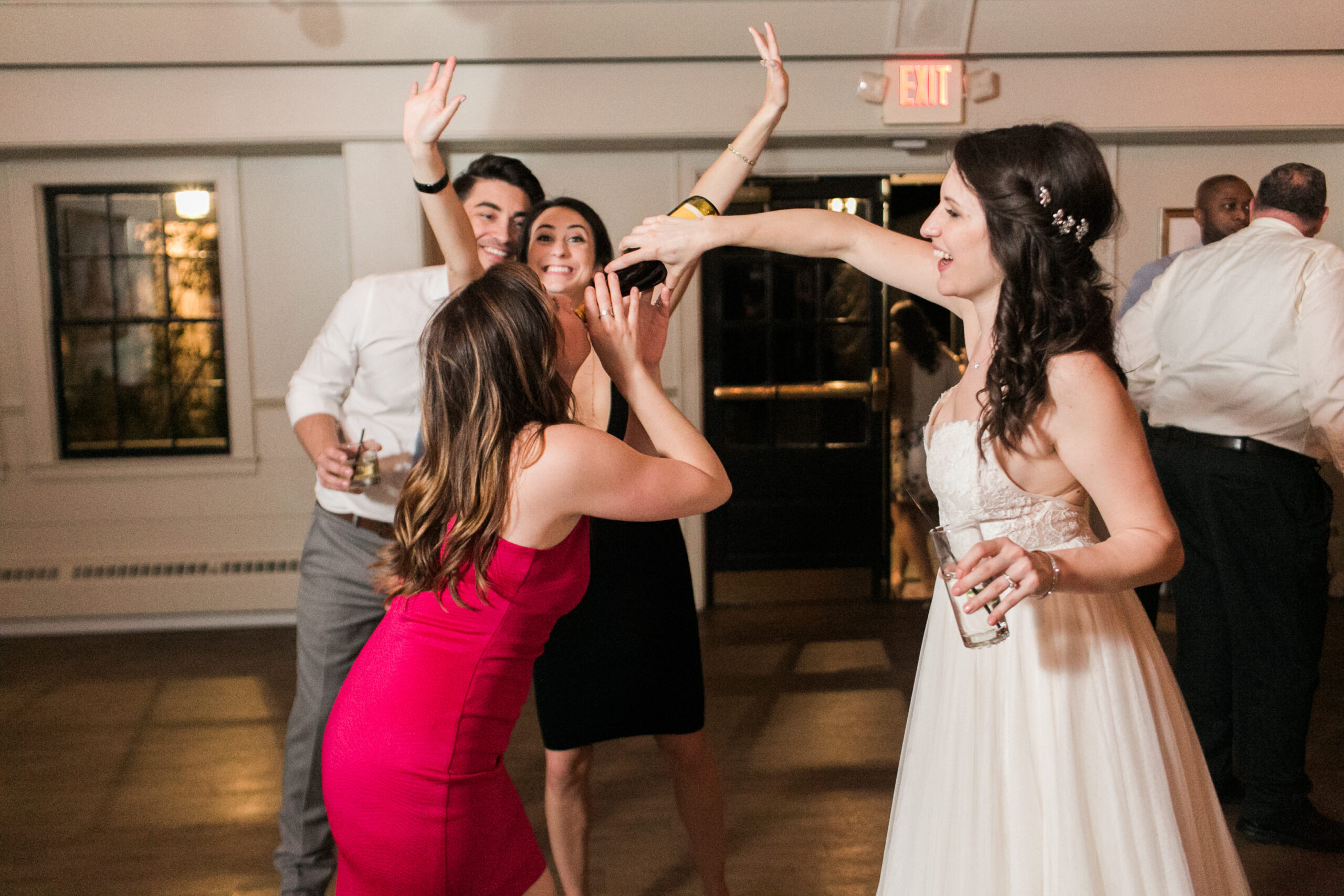 Fun woman in red dress waiting for champagne to be poured into her mouth by bride in white dress Latitude 41 Mystic