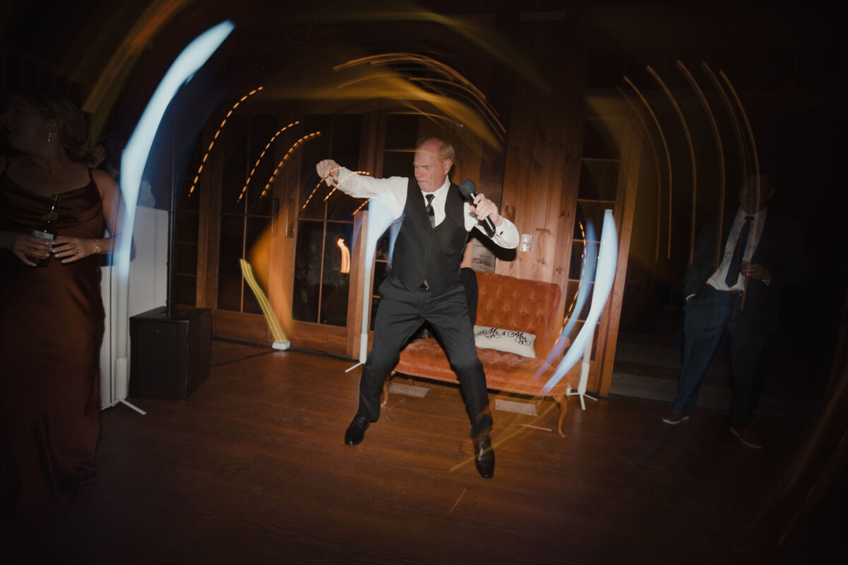 Father of bride dancing with microphone in hand during a lip sync performance at her daughters wedding at The Preserve at Chocorua in Tamworth NH
